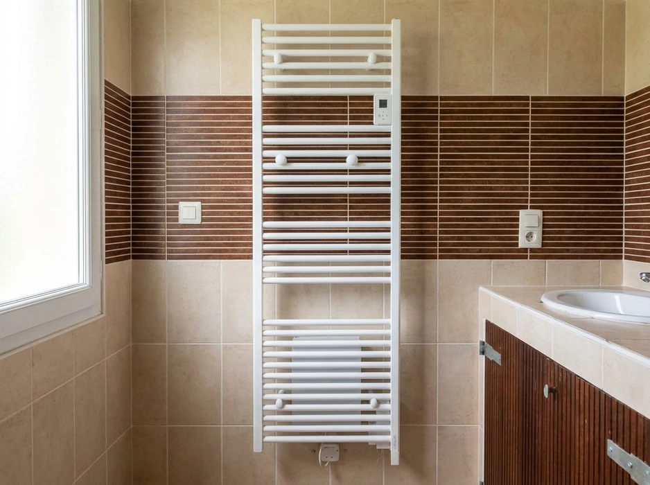 Salle de bain carrelée beige et marron avec un sèche-serviettes électrique blanc vertical à barreaux, thermostat numérique intégré