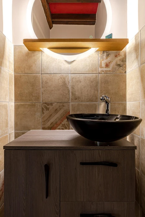 Salle de bain moderne avec vasque à poser noire brillante en céramique, montée sur meuble bas en bois foncé à deux portes avec poignées noires