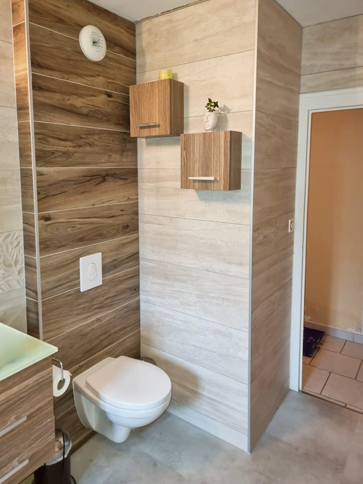 Salle de bain moderne avec WC suspendu, carrelage imitation bois et pierre travertin