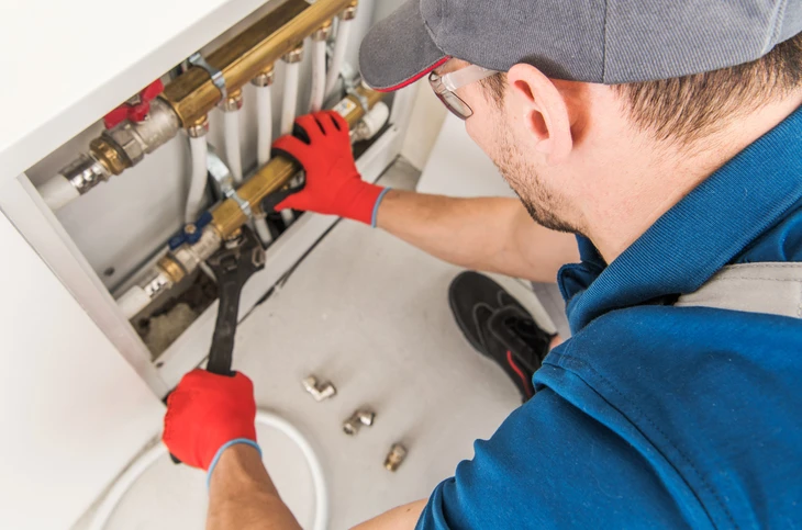 Technicien en plomberie intervenant sur installation de chauffage domestique dans local technique résidentiel