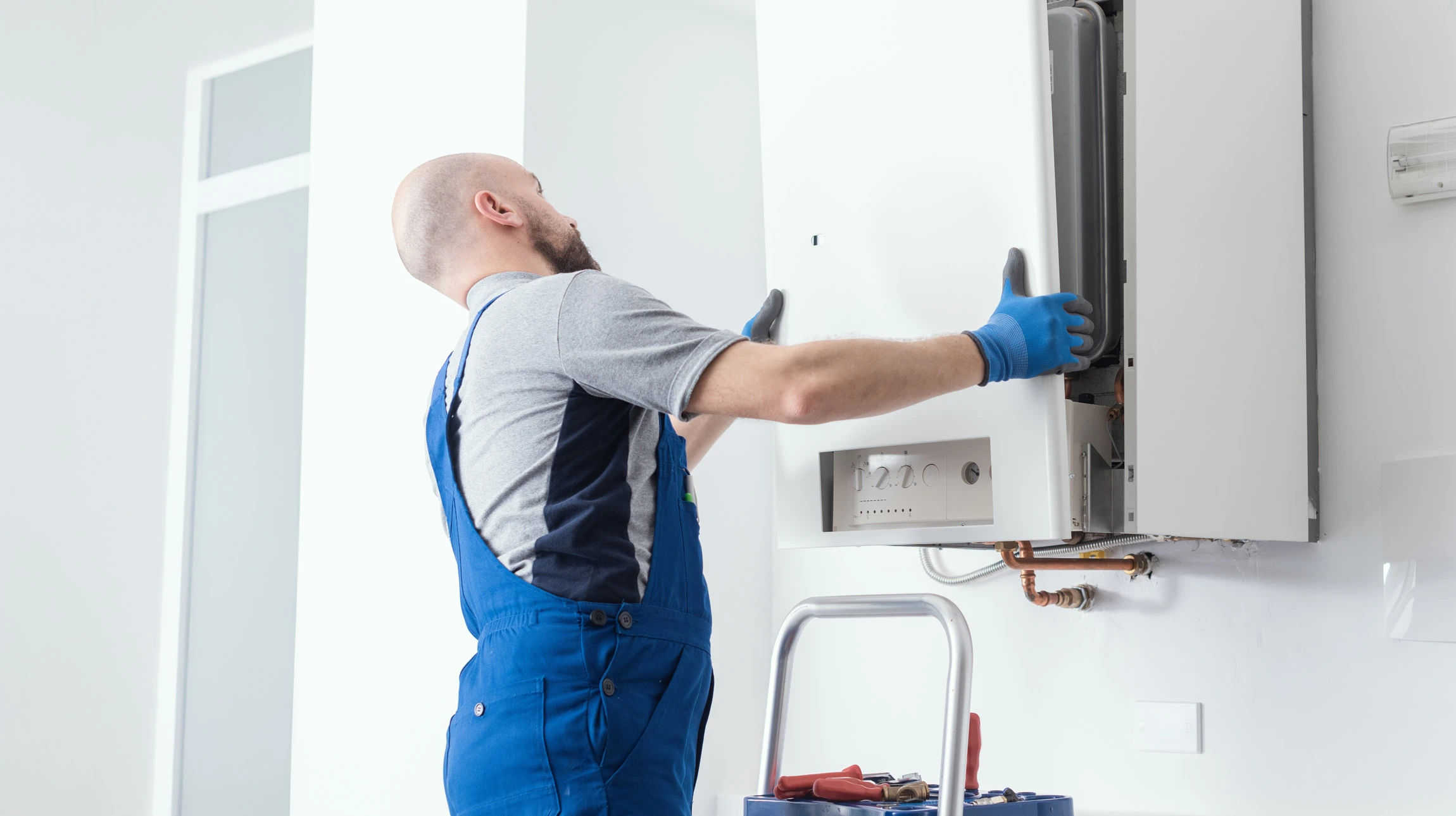 Photographie d'une installation de chauffe-eau thermodynamique complète et moderne, fixée au mur d'une salle technique ou chaufferie. Le système doit être clairement reconnaissable avec son bloc compresseur thermodynamique et ses tuyauteries de raccordement en cuivre. L'image doit montrer un environnement professionnel, bien éclairé, mettant en avant une installation de qualité exécutée par un professionnel. La photo doit être prise de manière à montrer l'ensemble du dispositif de façon claire et professionnelle, illustrant la compétence technique et la modernité de la solution.