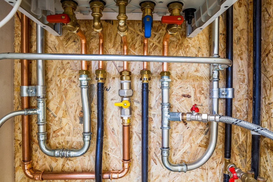 Vue d'ensemble d'une installation de chauffage et plomberie intégrée dans un local technique, montrant à la fois une chaudière moderne (ou une pompe à chaleur) et un système de tuyauterie en cuivre avec collecteur de distribution interconnectés. L'image doit montrer clairement les deux systèmes travaillant ensemble, avec des raccords professionnels visibles, prise de vue assez large pour laisser voir l'ensemble cohérent de l'installation, éclairage naturel ou professionnel, aspect soigné et professionnel.