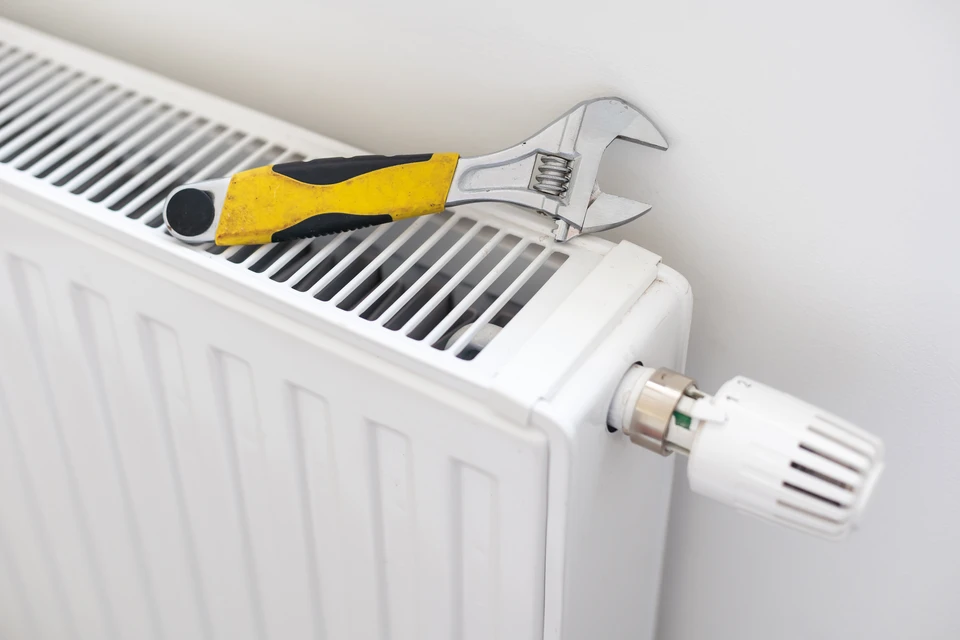 Technicien en plomberie travaillant dans une chaufferie résidentielle, ajustant une canalisation avec une clé à molette rouge