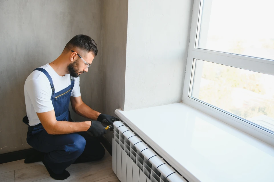 Un technicien en chemise à carreaux ajuste les paramètres d'une chaudière murale domestique tout en consultant un carnet de maintenance