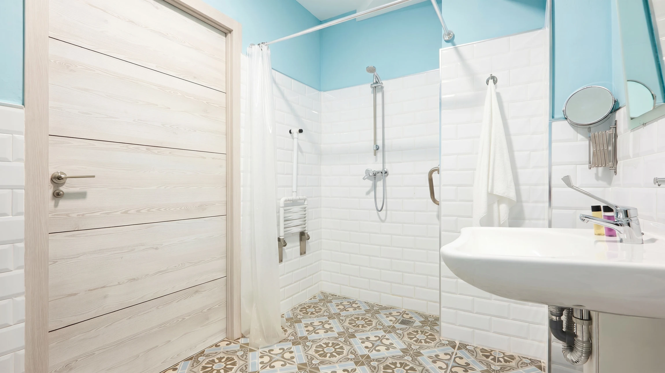 Toilettes PMR dans salle de bain carrelée beige avec WC suspendu équipé de barres d'appui latérales rabattables